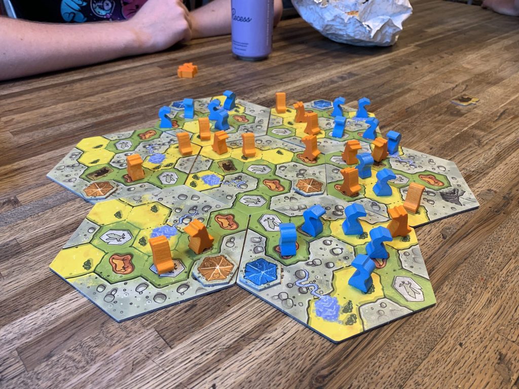 The Great Plains game board in the midst of a game, blue and orange pieces set on hexagonal spaces across the table.