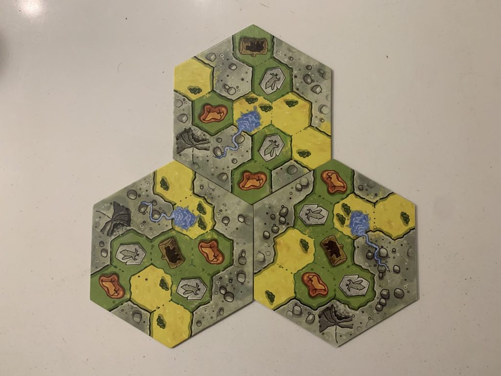 A close-up image of three of the board's modular hexagonal tiles, each subdivided into plains, mountains, and grasslands.