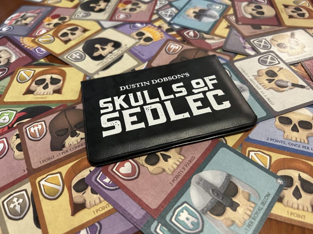 The Skulls of Sedlec wallet, set upon a sprawling pile of Skulls of Sedlec cards.