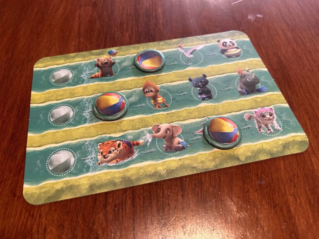 A player board, with the three beach ball tokens at varying stages of crossing the board.