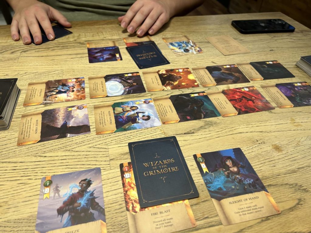 The table in the middle of a game. There are ten cards out in the market, in the middle of the table, and each player has spells down in front of them.