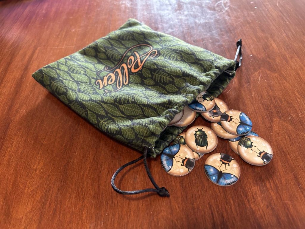 The pollinator token bag is a green cloth bag, shown here with a number of the circular pollinator tokens spilling out onto the table.