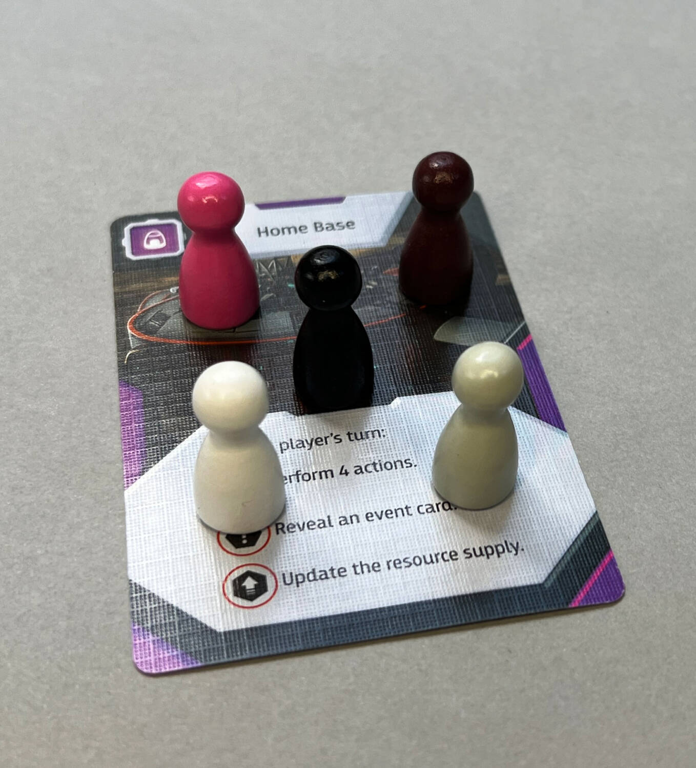 All five player tokens on the Home Base card. The black (center) and brown (back right) require good lighting to distinguish between the two, as do the white (front left) and gray (front right).