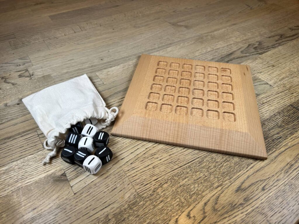 The board, a handsome wooden square that rises to a pleateau in the middle, together with the black and white dice, which come in a white cloth bag.