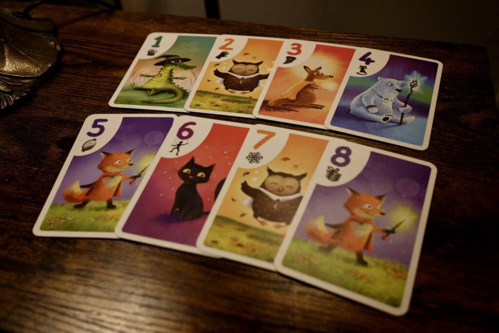 The eight different cards in Zing-a-Zam, laid out in numerical order. The five player characters include an alligator, an owl, a kangaroo, a polar bear, and a fox. There's also a sixth, neutral card, the cat. All of the illustrations are rendered in soft pastel colors.