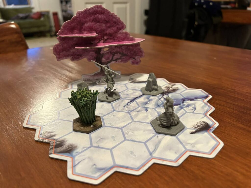 A wider shot of the board, with two warriors, several pieces of terrain, and a sakura standee in the far back.