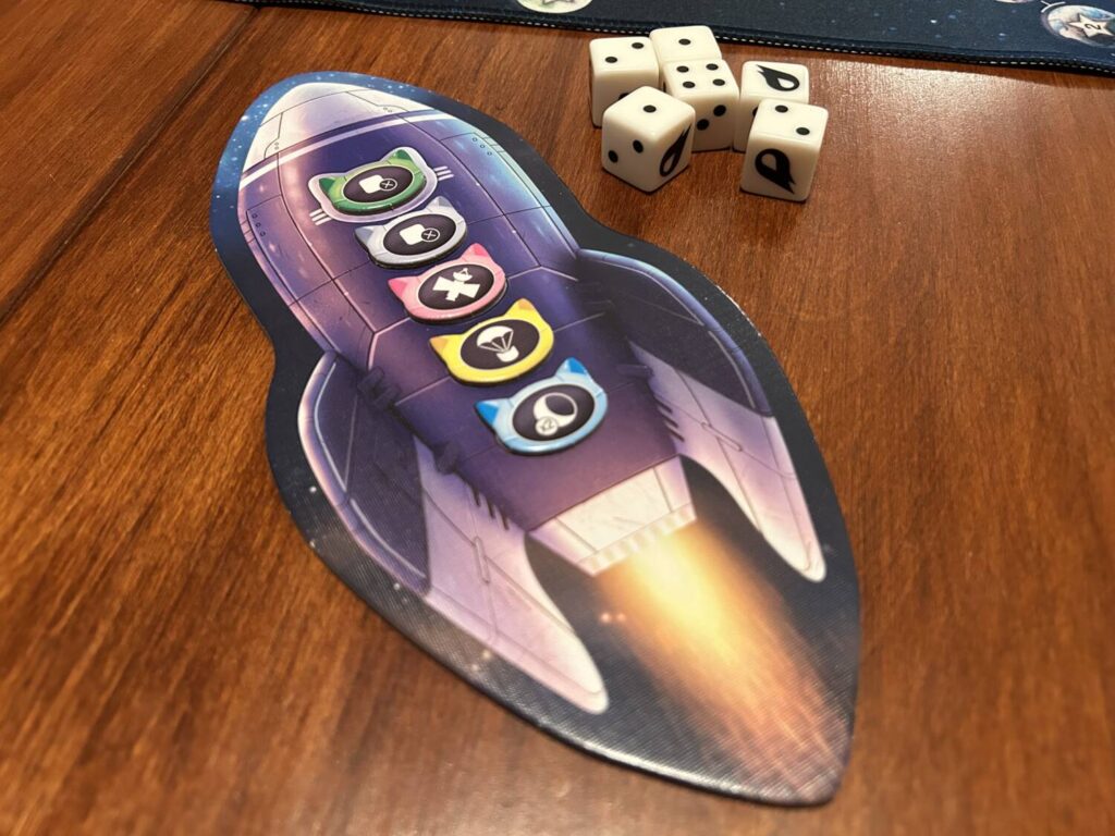 The rocket-shaped board that holds the cats players have sent on the current mission, next to six large white dice.