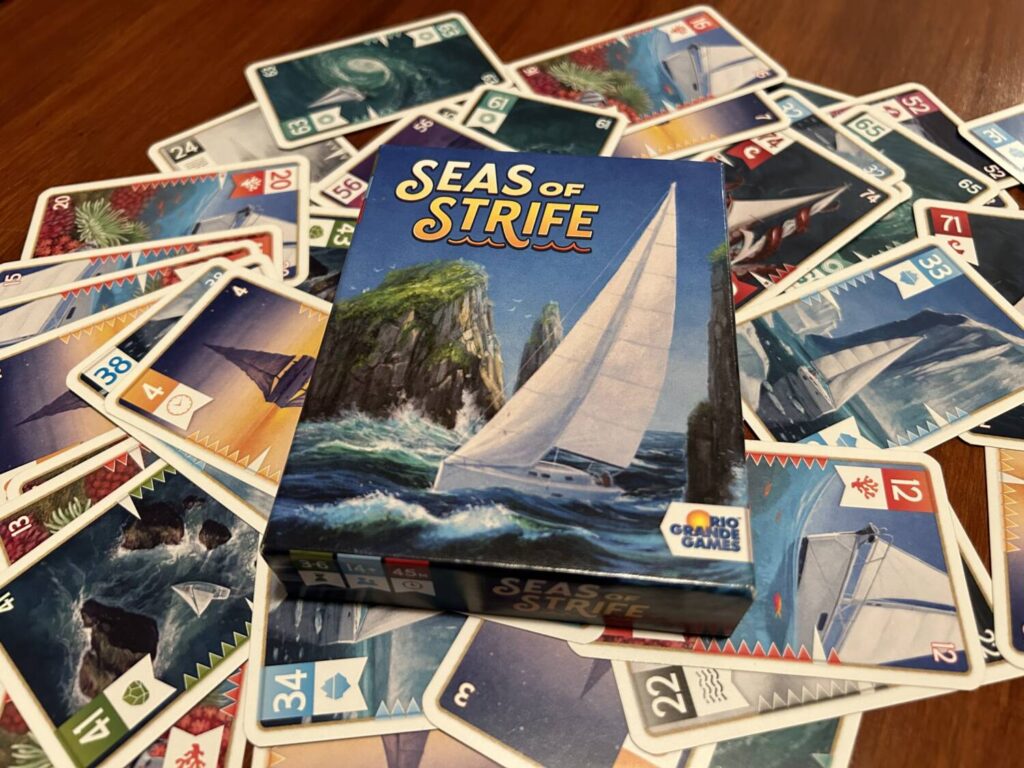 The Seas of Strife box, which shows a sail boat, set on the table with the cards spread underneath it.