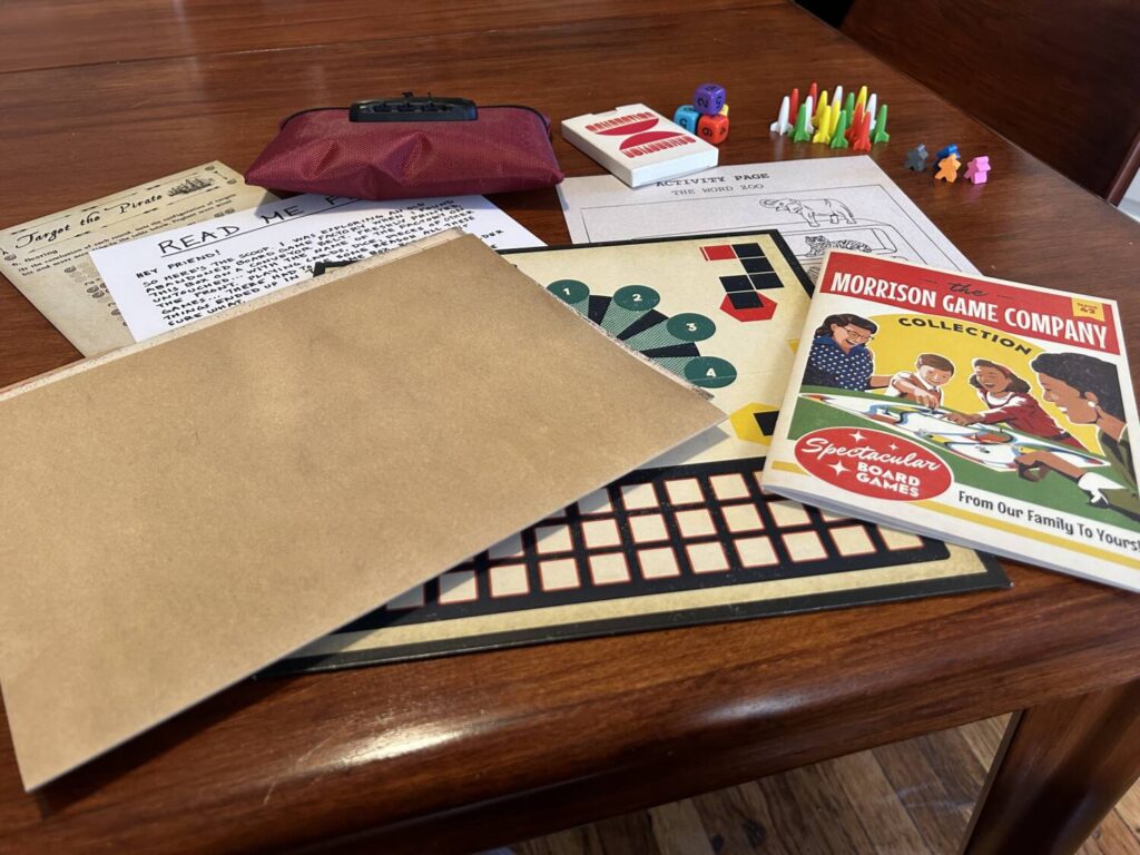 Myriad objects spread across the table, including a file folder, a catalogue, a board, dice, a locked pouch, a deck of mysterious cards, and more.