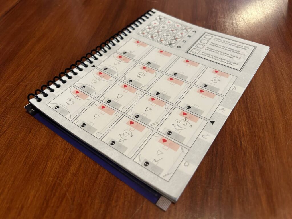 A spiral bound notebook with a grid replicating the card layout on the table.