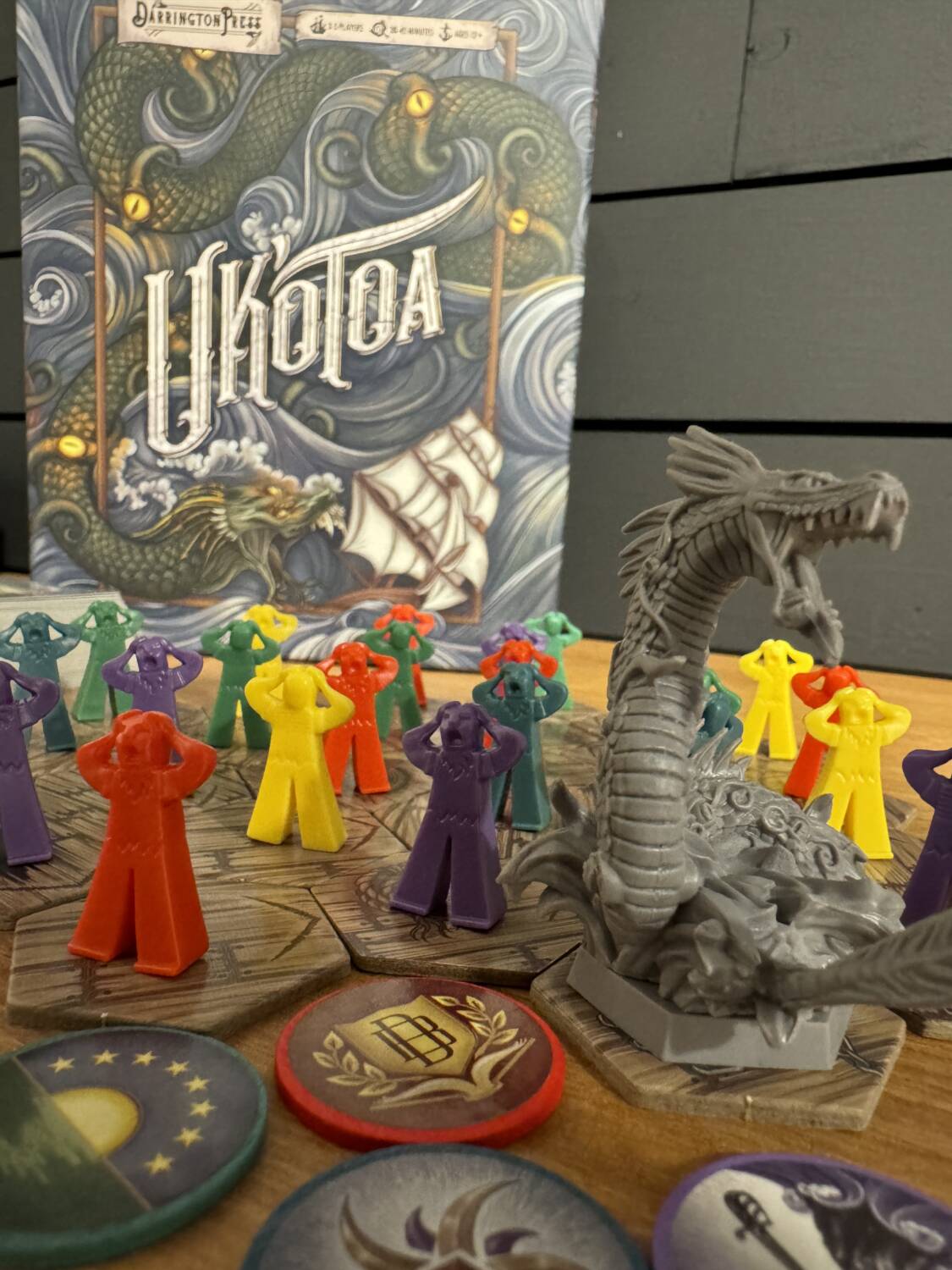 Uk'otoa Board Game components showing the miniature Uk'otoa and multi-colored sailors in front of the game box.