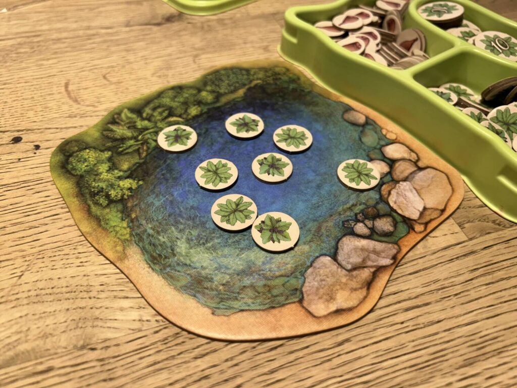 The feeding pool, a board decorated with a watering hole, featuring a number of vegetation tokens.