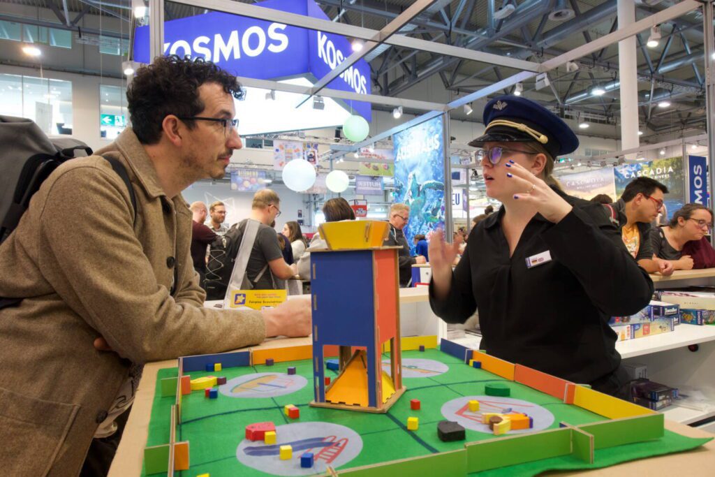 Jim speaks to a woman dressed in an airline pilot uniform at the KOSMOS booth.