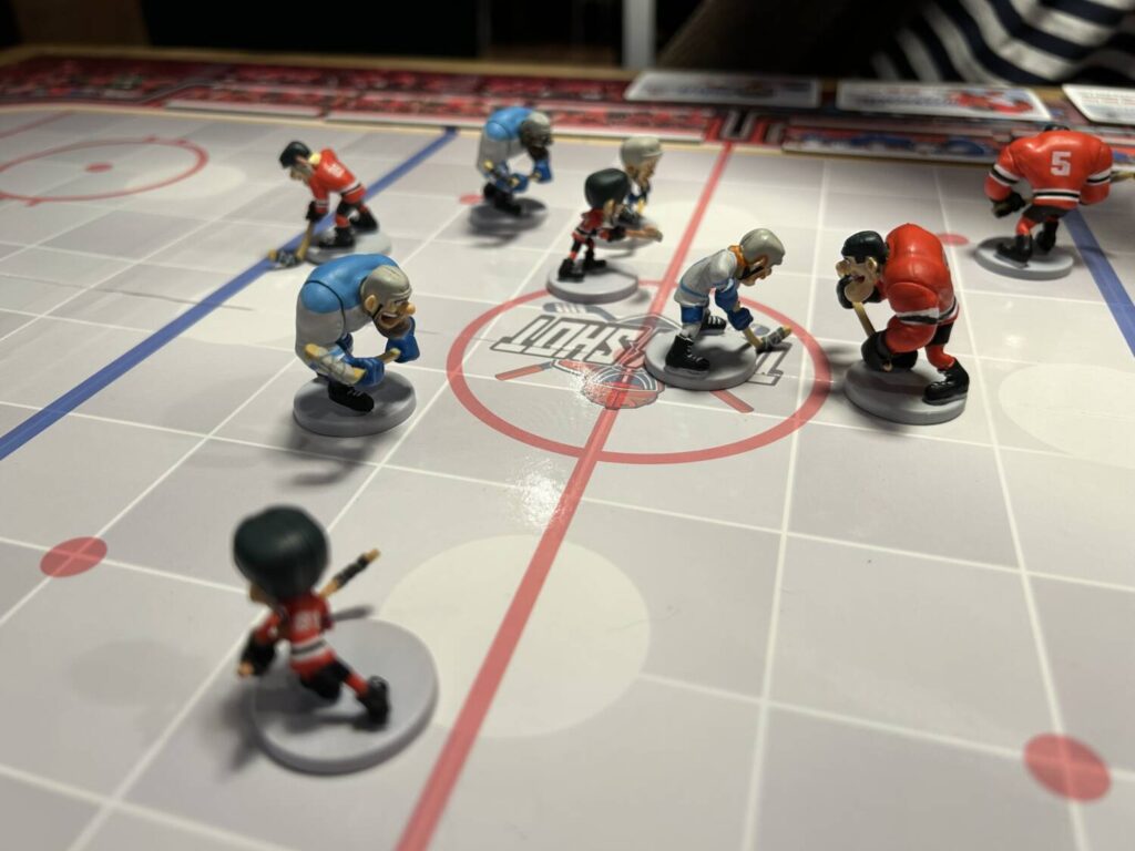 A group of painted plastic miniatures playing hockey, on a rink that's been divided into a grid.