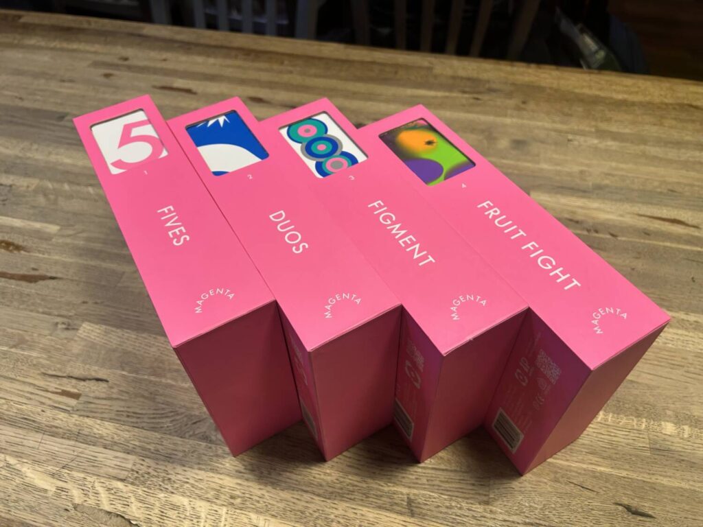 The four bright magenta slipcases. Each features the game's name in a white font, and a window cutout that highlights a bit of the game's art on the interior box.