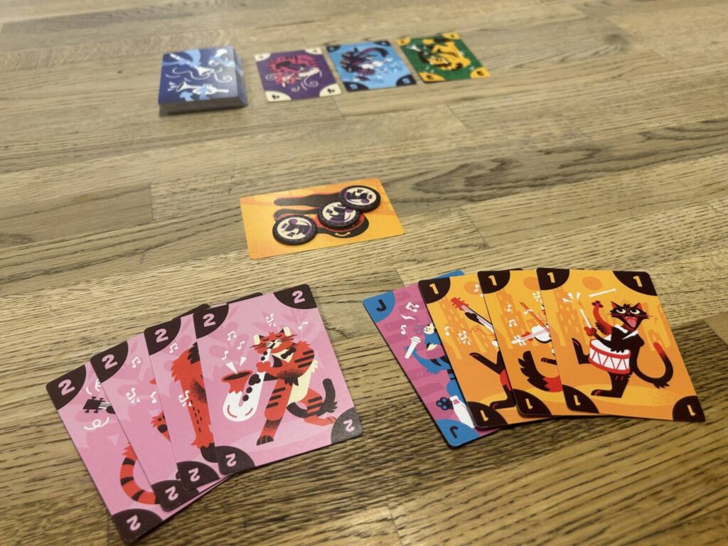 Two sets of four cards melded to the table, with corresponding score tokens set in front of them. The card market can be seen further up the table.