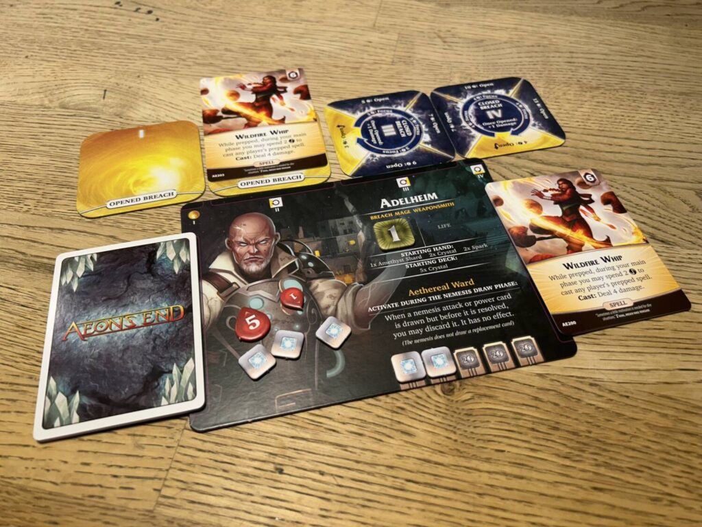 A rectangular player board. The draw pile is to the left, the discard pile is to the right. Droplet-shaped life tokens litter the board. Four squares, in yellow and blue, line the upper edge of the board.