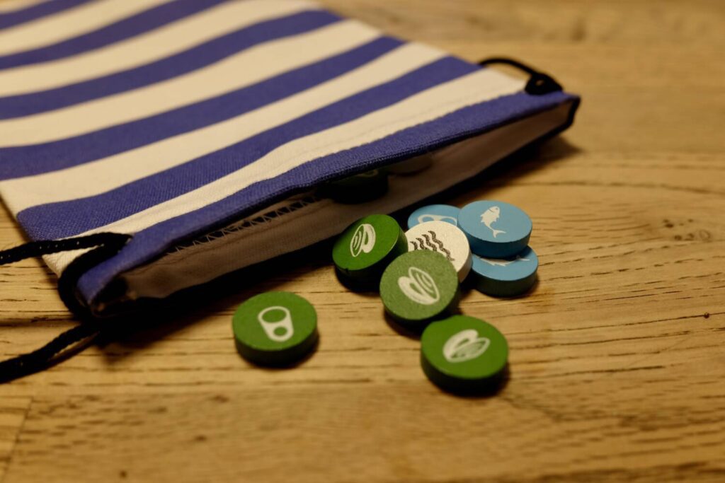 A blue-and-white striped cloth drawstring bag, with wooden tokens spilling out onto a wooden table.