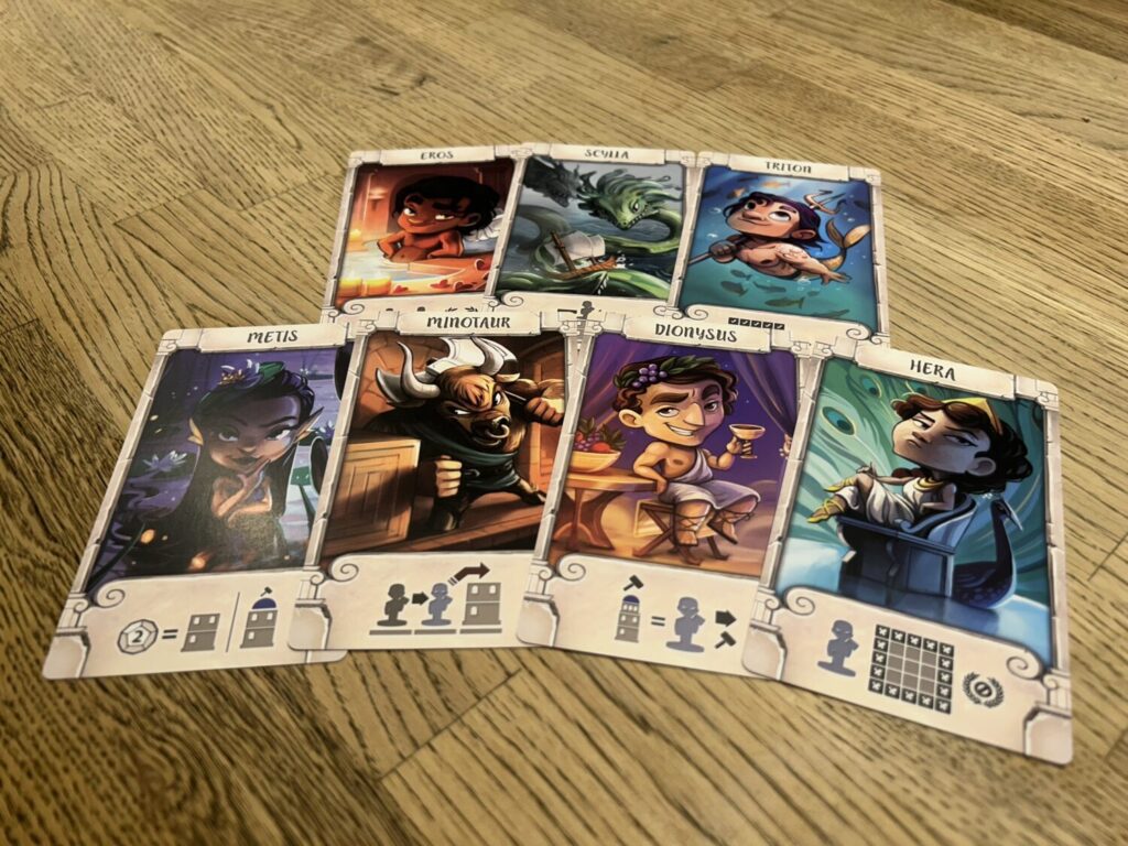 God cards laid on a table. Each god card has a large, full-color illustration taking up the majority of the card, with icons indicating the god's power along the bottom.