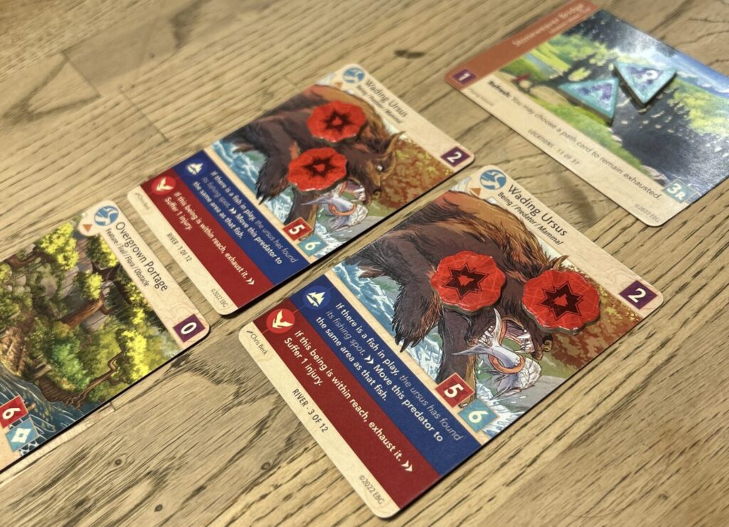 Several cards on a wooden table, including two with damage tokens.