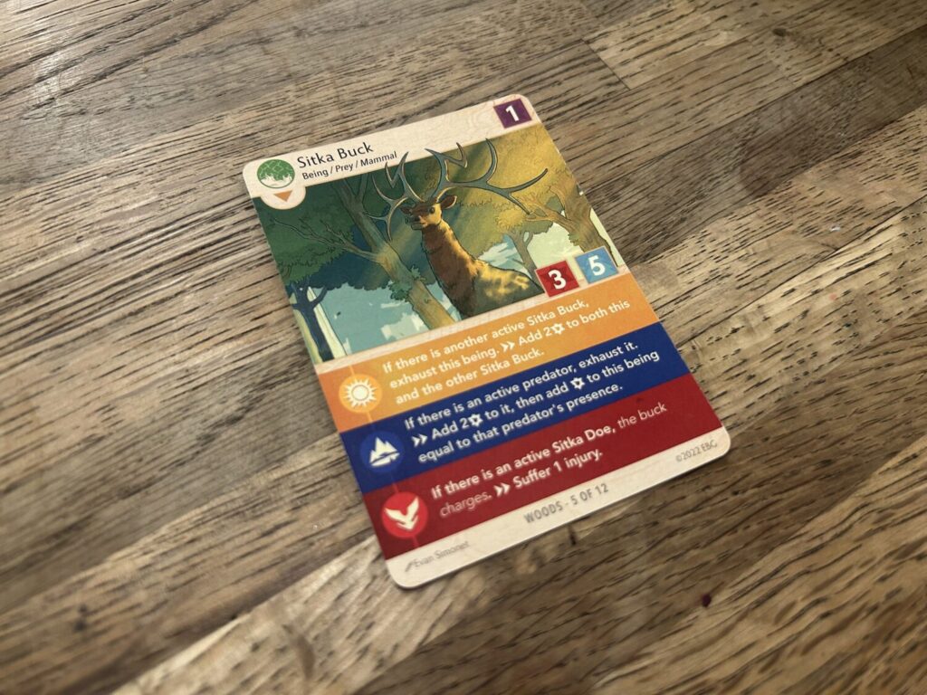 A card sitting on a wooden table. The card shows an illustration of a deer-like animal. Below the illustration are three text boxes, each corresponding to a different symbol.