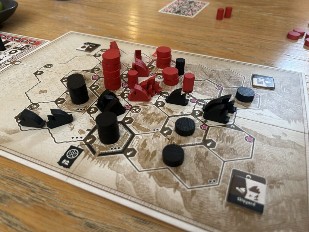 A crowded board near the end of a game. The board, which includes water and land spaces, is divided into hexagons. Wooden boats and discs that represent troops populate the map.