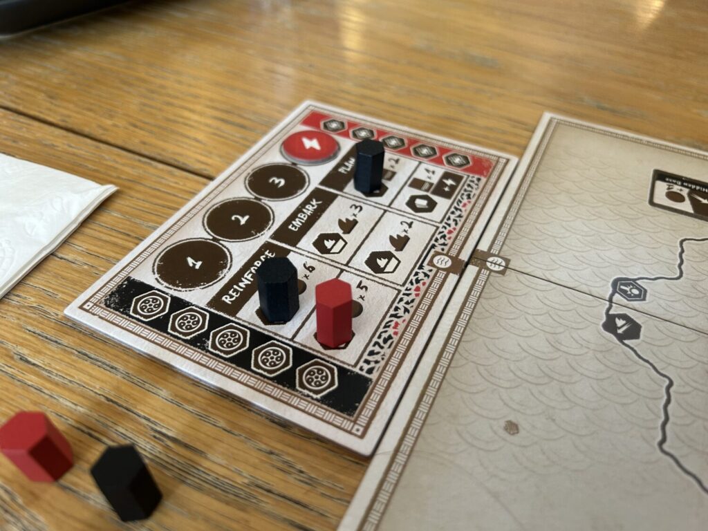 The action selection board, which sits adjacent to the main board. It is decorated with six spaces, two for each of three primary actions. Wooden hexagonal cylinders occupy some of the spaces.