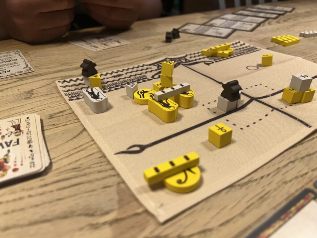 A tan board made of cloth, with two thick black lines bisecting the board, one in each direction. The board is filled with yellow and white wooden pieces in various arrangements.