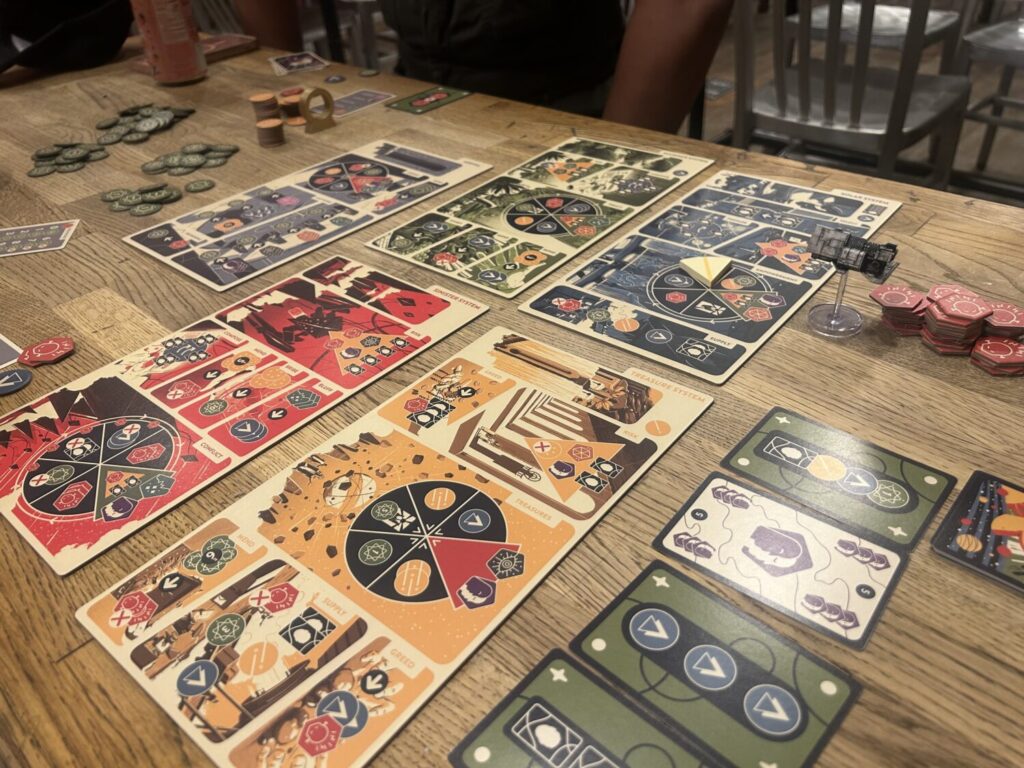 A number of rectangular boards sit on the table in a grid. A plastic spaceship marks the current location for the players.