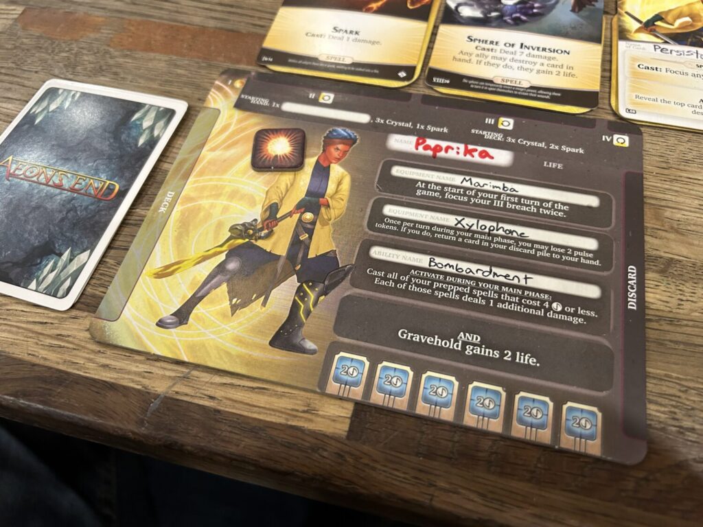 A rectangular playing board on a wooden table. The palyer board includes a number of stickers that have been added over the course of multiple sessions.