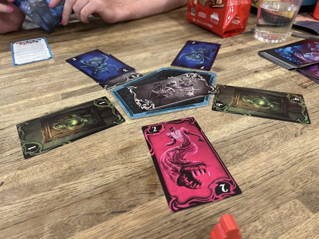 A pentagonal board sits in the middle of the table, with one card radiating outwards from each of its edges.