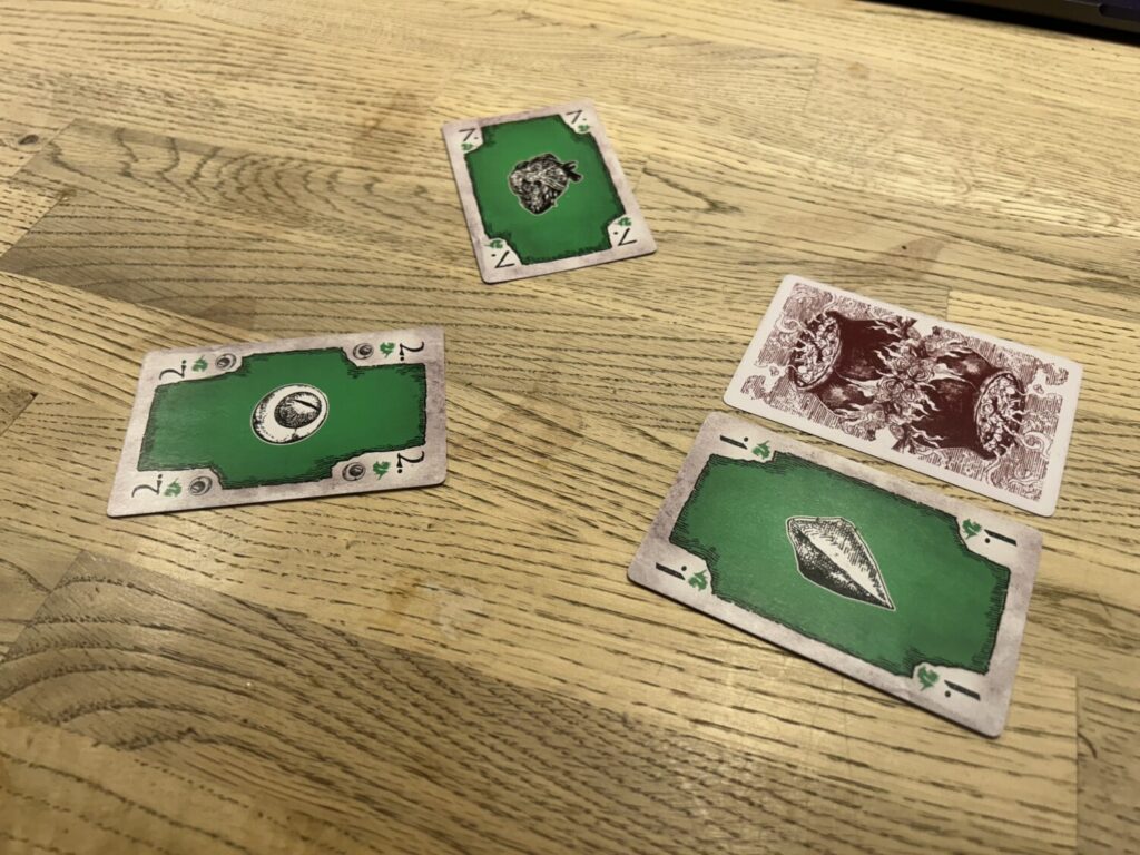 Four cards on a wooden table. Two of the cards are next to one another. One is face down. The other is faceup, and green. The two other cards, also faceup, are also green.