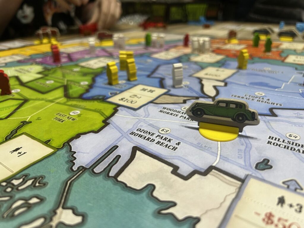 The board later in the game. Mobsters occupy a variety of areas, and a car standee stands in the middle of a region.