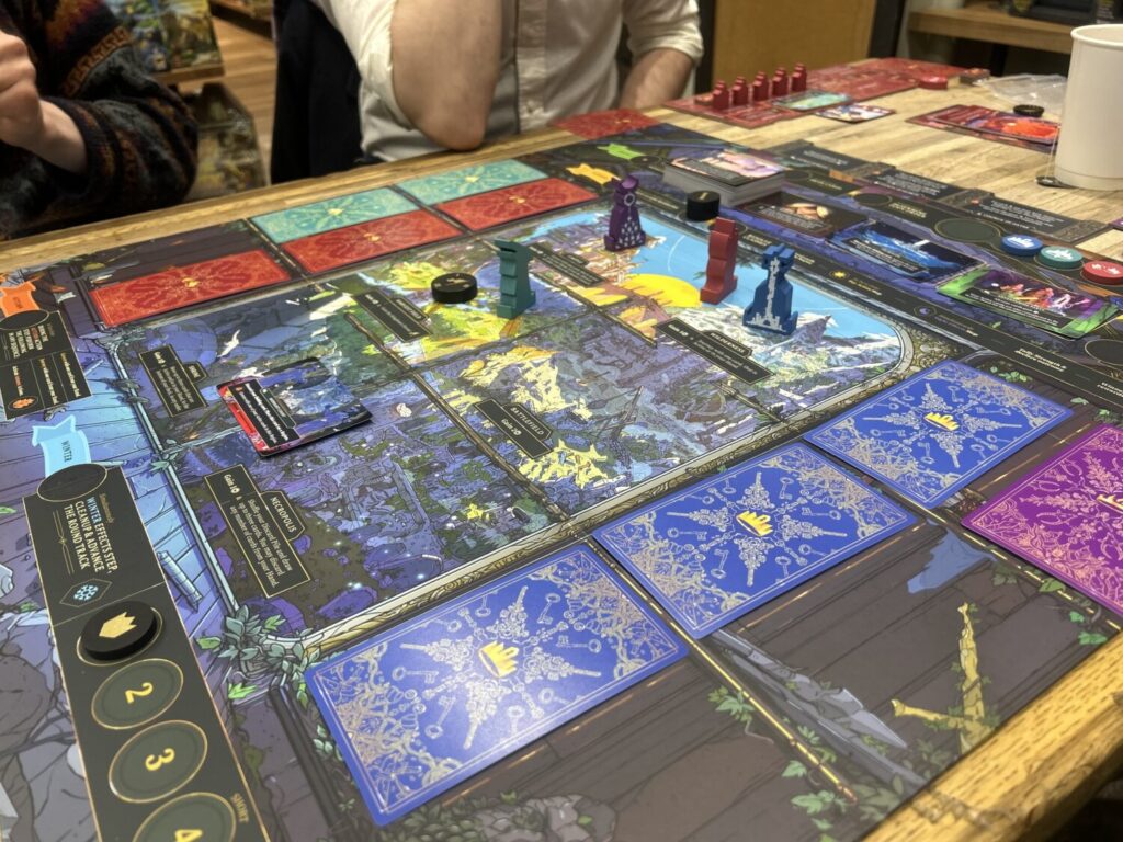 A large board, primarily decorated with the panes of a large window looking out onto the kingdom. There are wooden figures on several of the panes, and facedown cards next to each of the three rows in the three by two grid.