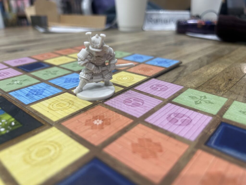 A grey plastic miniature of a red panda in samurai armor prowls the board.